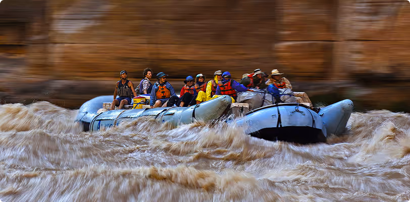 Rafting team navigates turbulent whitewater rapids with rocky canyon walls